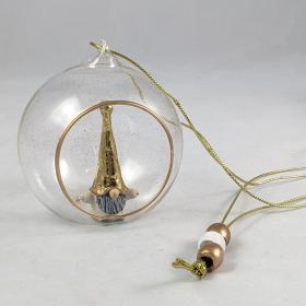 Transparent globe that has specks of gold glitter has a small opening in the front and shows a gold and white tomten inside the globe. a metallic string is connected to the the top and shows three beads on the strand. 
