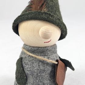 Very folk style tomte dressed in green and gray, holding a cross body tan satchel. 